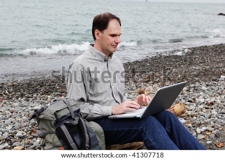 Man with backpack and laptop sitting on a log at the beach