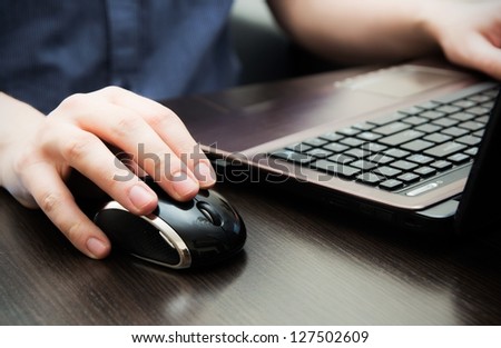Human hand on computer mouse. Laptop on desk.