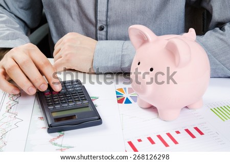 Man calculates money. Piggy bank and business documents on desk