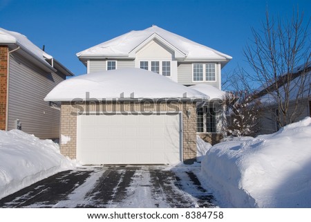 contemporary 2 floor beige brick house with garage in front; heavy snow; driveway in foreground; frontal view; deep blue sky