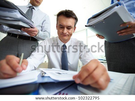 Responsible accountant doing financial reports being surrounded by business partners with huge piles of documents