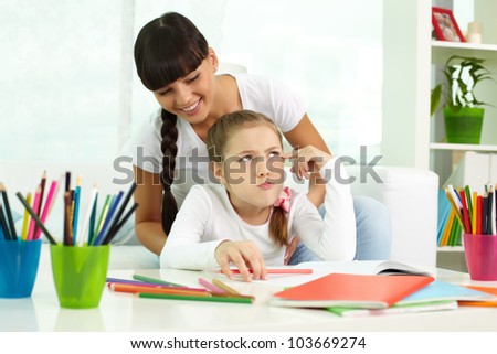 Portrait of cute girl thinking while drawing with colorful pencils with her mother near by