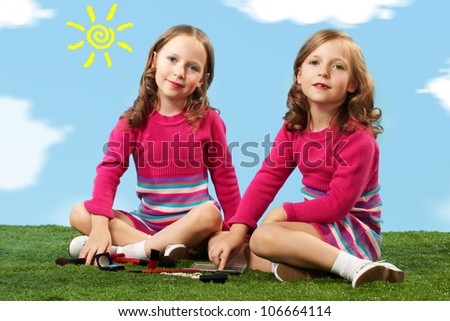 Portrait of two smart girls in smart clothes sitting on lawn and looking at camera