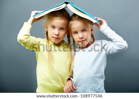 Portrait of lovely twin girls holding open book over heads