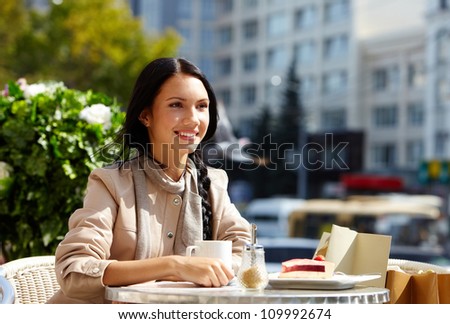 Image of happy female in open air cafe having coffee with cake in urban environment
