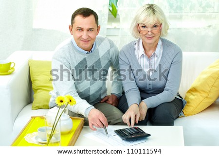 Portrait of mature man and his wife looking at camera while making financial revision at home