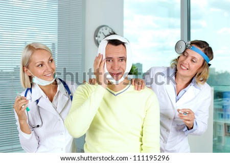 Portrait of two careful female doctors giving first aid to male patient with toothache in hospital