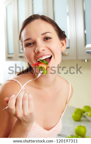 Portrait of a girl eating salad with fork and looking at camera