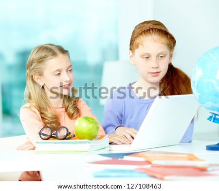 Portrait of smart schoolgirls sitting in classroom in front of laptop