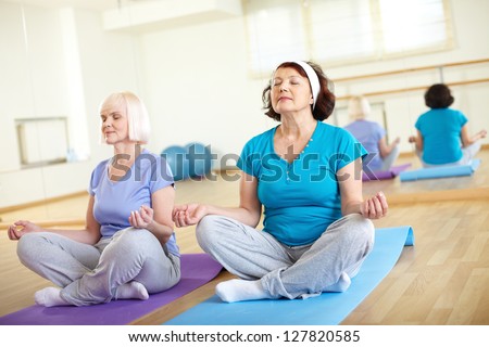 Portrait of two aged females doing yoga exercise in sport gym