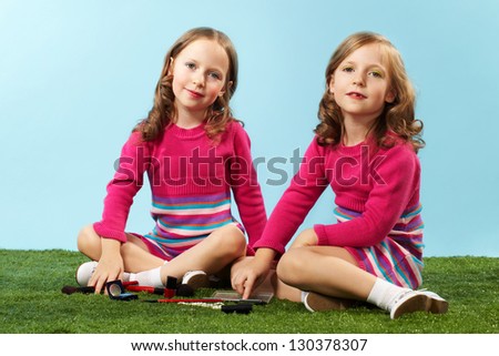 Portrait of two smart girls in smart clothes sitting on lawn and looking at camera
