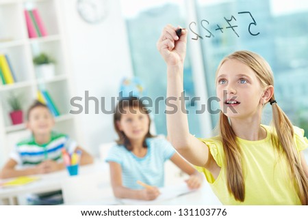 Portrait of lovely girl doing sums on transparent board with schoolmates on background