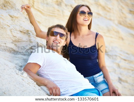 Young people in sunglasses leaning against sandy wall on the beach
