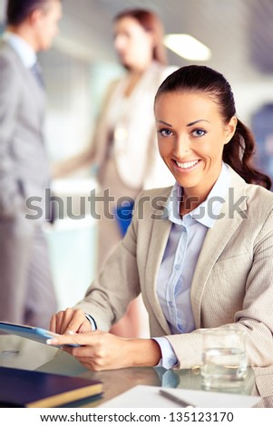 Portrait of confident employee working with touchpad on background of working colleagues