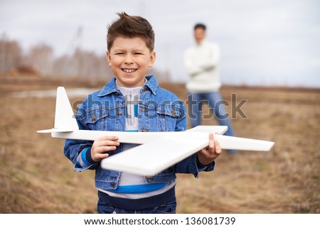 Photo of happy kid with toy airplane looking at camera with his father on background