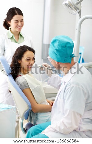 Cheerful patient receiving dental care from a friendly doctor and his assistant