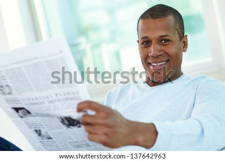 Image of happy young African man looking at camera while reading newspaper