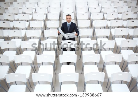 Portrait of confident businessman with newspaper sitting on one of chairs
