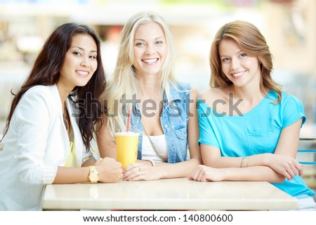 Portrait of three happy girls looking at camera while having drink after shopping