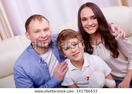 Portrait of happy family of three sitting at home and looking at camera
