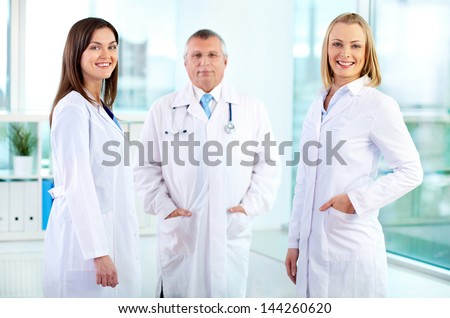 Portrait of happy nurses looking at camera with mature doctor behind