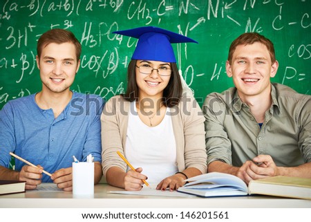 Portrait of three smart students looking at camera with chalkboard on background