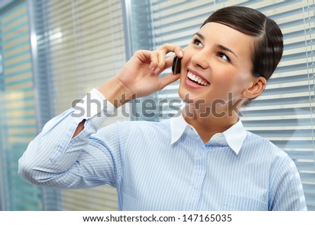 Image of young pretty secretary talking by cellular phone in office