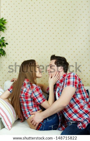 Amorous couple sitting on sofa, looking at one another and flirting