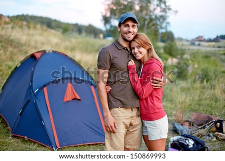 Photo of resting couple looking at camera in the countryside with tent on background
