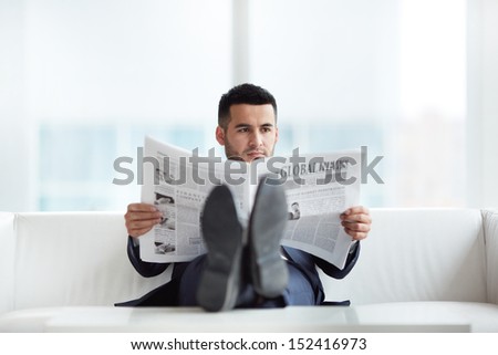 A young businessman on sofa reading newspaper in the office