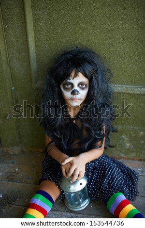 Portrait of Halloween girl with lantern sitting on the floor of dilapidated house