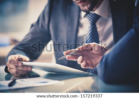 Photo of Image of two young businessmen using touchpad at meeting