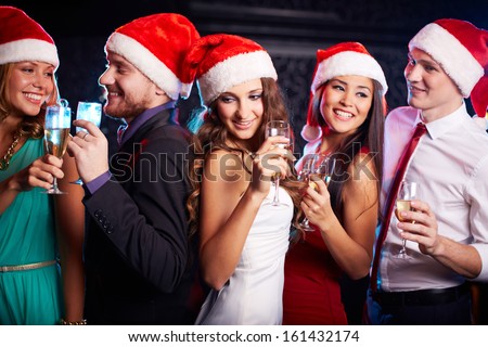 Company of friends in Santa caps holding flutes of champagne at Christmas party