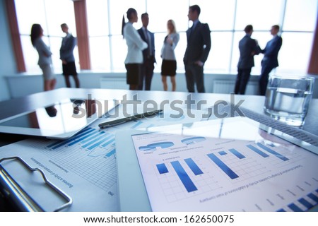 Close-up of business document in touchpad lying on the desk, office workers interacting in the background