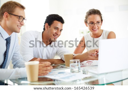 Portrait of successful businessman pointing at laptop screen while explaining something to his colleagues at meeting