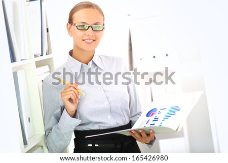 Portrait of elegant businesswoman looking at camera while working with papers in office