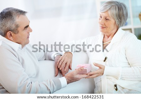 Portrait of mature woman taking small giftbox given by her husband