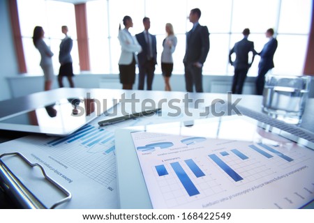 Close-up of business document in touchpad lying on the desk, office workers interacting in the background