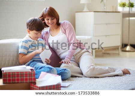 Portrait of cute boy opening envelope with his mother near by at home