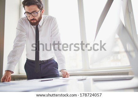 Young businessman standing by the window in office and working with papers