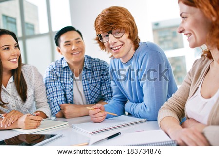 Group of smart groupmates sitting at lesson, guy in eyeglasses looking at camera