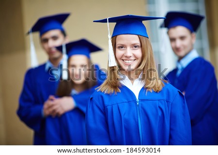 Friendly students in graduation gowns looking at camera with happy girl in front