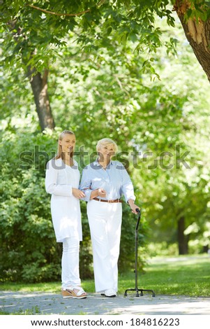 Pretty nurse and senior patient with walking stick having a walk in park
