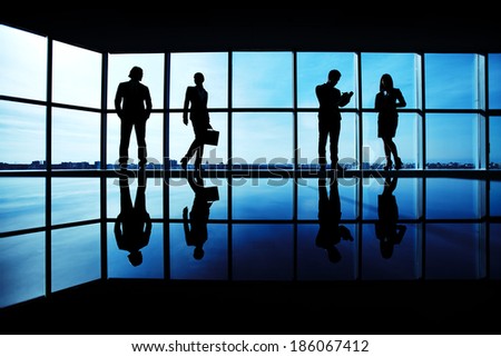 Silhouettes of several office workers standing on background of window