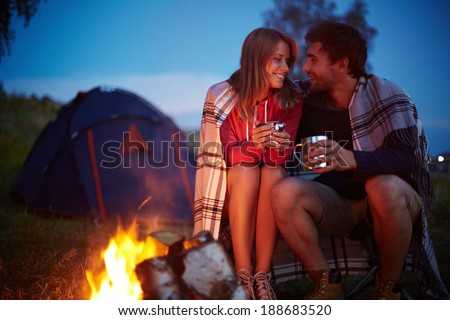 Young couple sitting by the fire and drinking tea outside