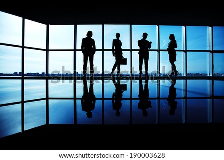 Silhouettes of several office workers standing on background of window
