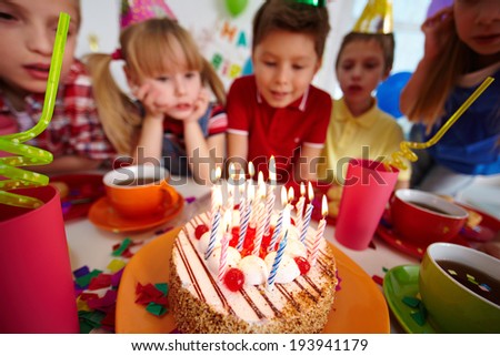 Group of adorable kids looking at birthday cake with burning candles