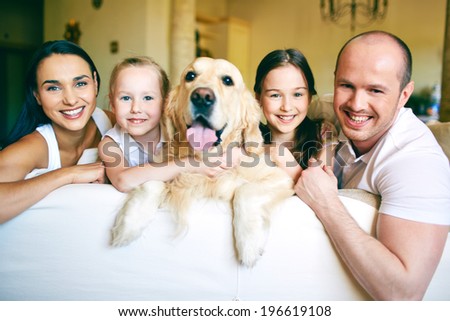 A young friendly family of four with pet looking at camera at home