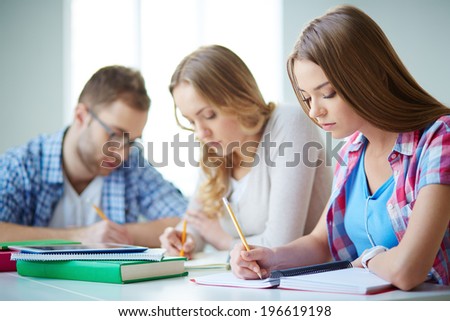 Smart girl carrying out written task with her groupmates on background