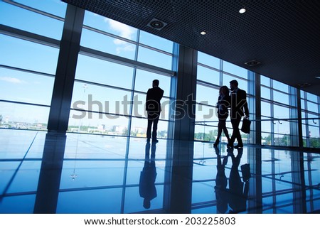 Silhouettes of office worker standing by the window and two business partners communicating while walking near by